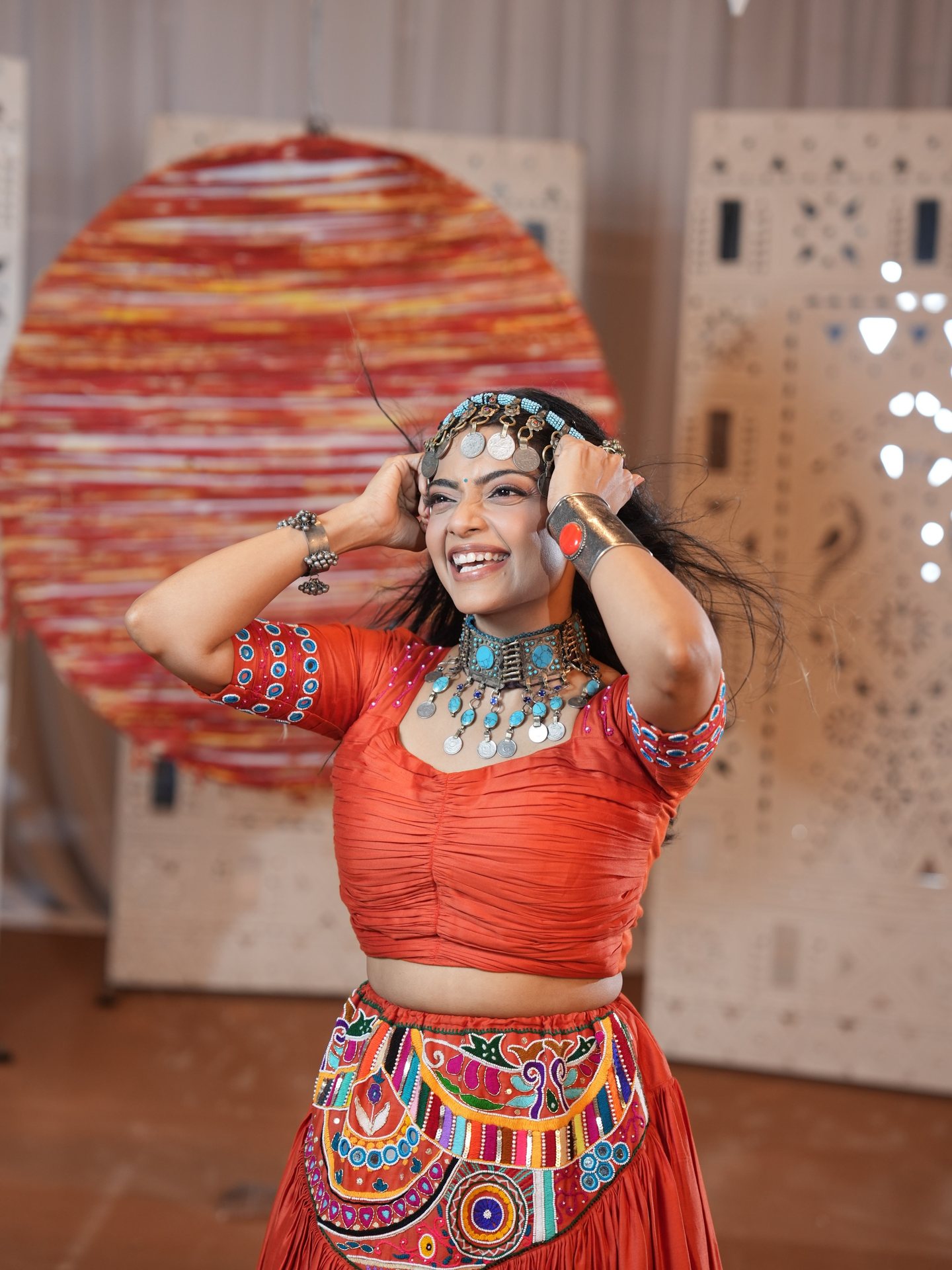 Pooja Kalyani laughing in an orange chaniya choli and silver coin headpiece