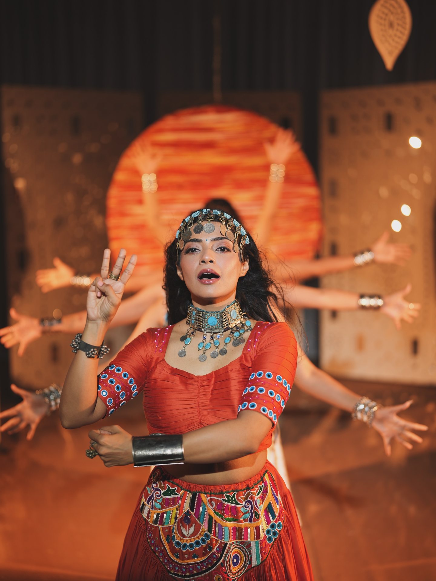 Pooja Kalyani mid-performance with dancers' arms fanning out behind her like a goddess